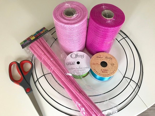 Materials needed to make a 6 inch deco mesh wreath: 14 inch wreath frame, light and dark pink rolls of deco mesh, rolls of green and blue ribbon, light pink pipe cleaners a/k/a chenille stems, and a pair of scissors. A tutorial. 