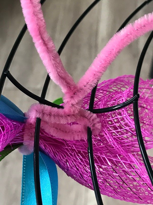 A close-up photo of crossed chenille stems showing how to add mesh to a wreath frame.